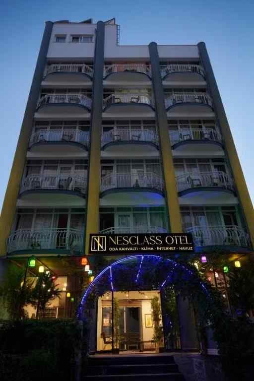 Nesclass Otel'in akşam ışıklarıyla aydınlanmış cephesi, balkonlar ve girişteki ışıklı kemer